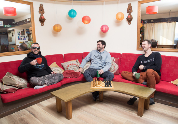 tres huespedes riendo sentados frente a un tablero de ajedrez